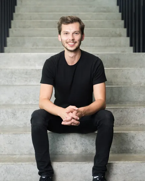 Phil sitzt lächelnd auf einer Betontreppe, in schwarzem T-Shirt.
